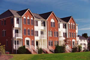 Exterior image of a three story, red brick and white vinyl siding apartment building at Sun Valley in Florham Park, NJ. There are several staircases leading to entry doorways, multiple balconies, and a lush green lawn.
