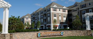 Exterior image of Xchange at Secaucus Junction in Secaucus, NJ. There is an entry wall with the community logo, with a large 4 story apartment building behind it.