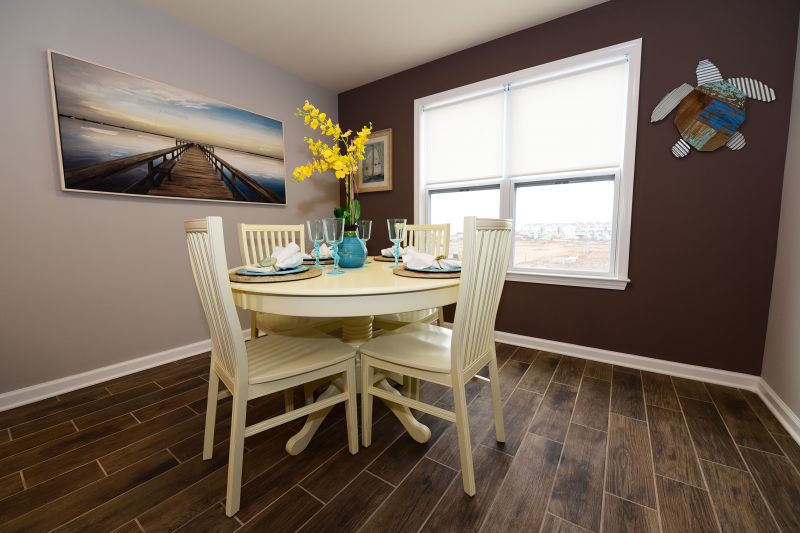 Photo of the dining room at Harbortown Breeze. There is a table for 4 with place settings and several pieces of wall art. Wood grain ceramic tile on the floor and a window to allow for natural light complete the room.