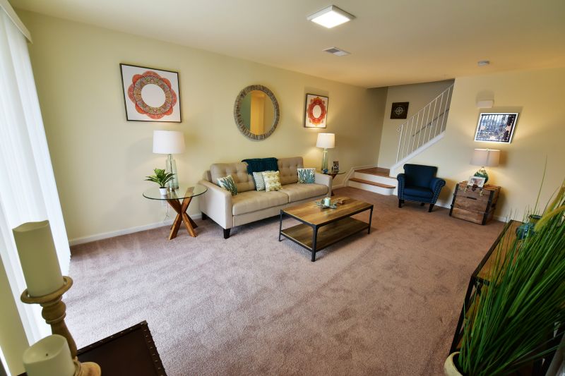Image of the living room in a Harbortown Breeze apartment showing wall to wall carpeting and several seating areas. Stairways in the back lead to another level of living space.