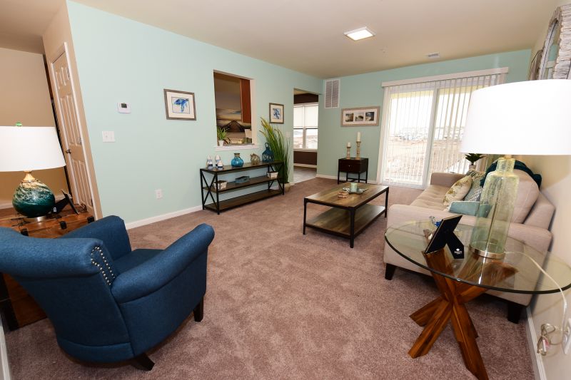 Photo of a living room at Harbortown Breeze with wall to wall carpeting. A sliding glass door leads to a balcony. There is a couch and chair, several end tables and a coffee table.