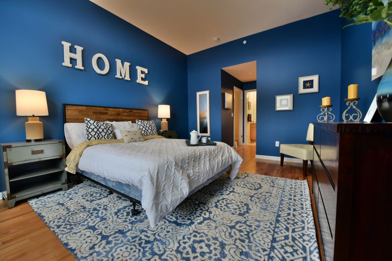 Harbortown Breeze photo of a Master Bedroom featuring hardwood floors. There is a queen sized bed with two end tables and a dresser. Various items decorate the room. There is a hallway leading to closets and a master bathroom.