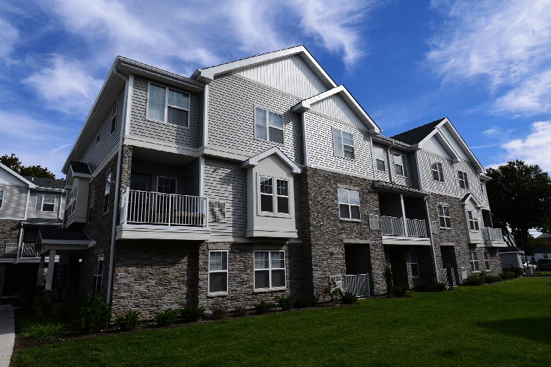 Hawthorne Square Exterior photo showing a brick and vinyl exterior with several balconies. Several bushes and trees highlight the landscape.