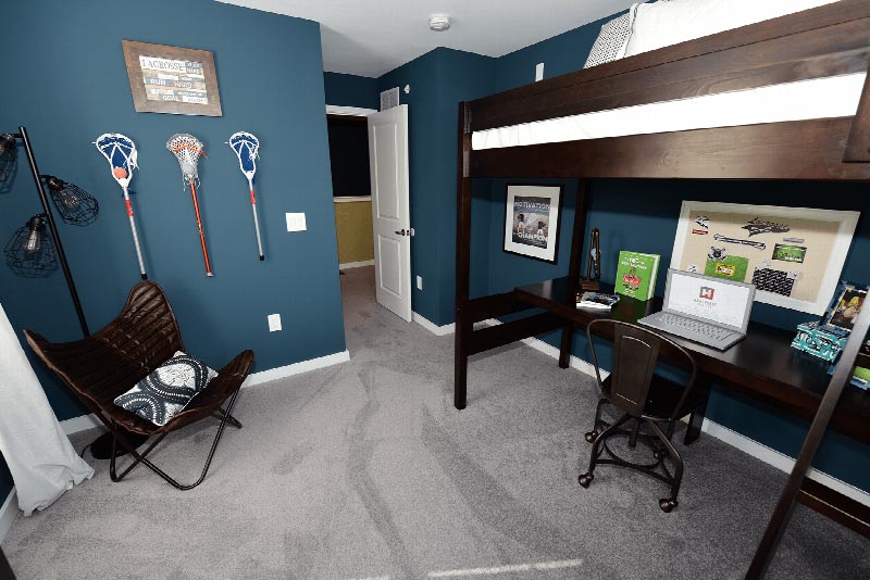 Hawthorne Square Bedroom photo showing a bunk bed with a desk underneath the bed with a chair. There is an additional chair in the corner next to a lamp. There are several decorations and pictures on the desk and walls.