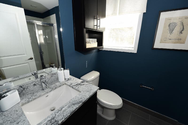 Hawthorne Square Bathroom photo showing an espresso vanity with a granite counter top and a mirror on the wall. There is a white toilet and a stand up shower. There is an espresso medicine cabinet next to the window and pictures on the wall.