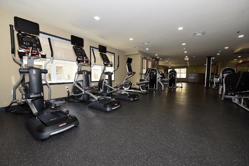 Hawthorne Square Gym photo showing three ellipticals, an exercise bike and various other exercise equipment. There are large windows to allow natural light to enter the room.