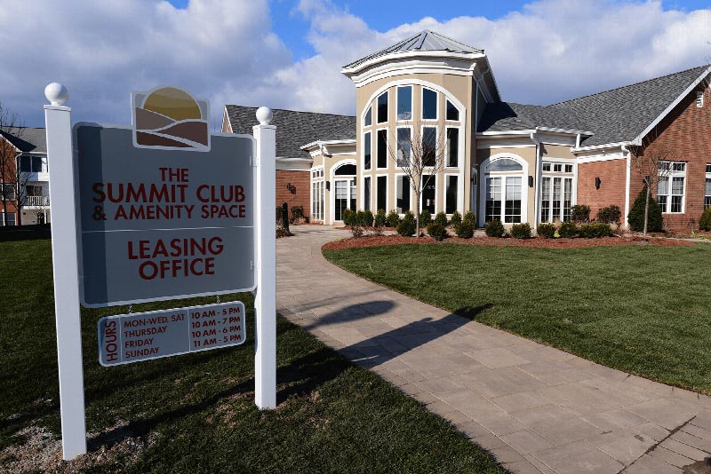 Photo of the front of the Summit Club at Sun Valley, showing the leasing office hours. A paver stone walkway leads to the entrance.