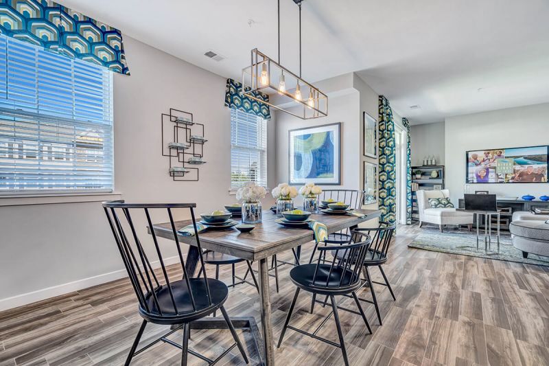 River Links interior photo of the dining room showing wood grain flooring, a table set for 6 people. There are 2 windows for letting in natural light. The room is open to the living room creating an inviting space.