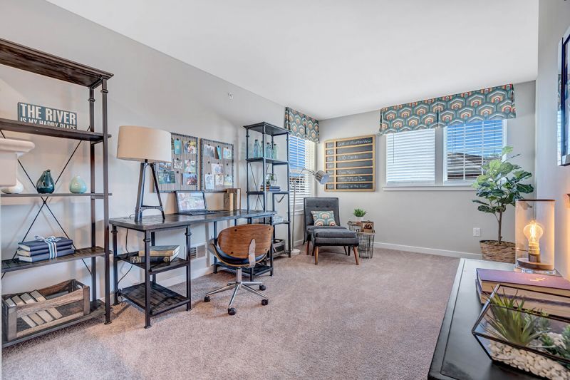 River Links interior photo of the den, home office showing a computer and desk, bookshelf, seating area and several windows for letting in natural light.