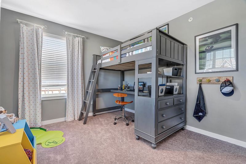 River Links interior photo of a kids bedroom showing wall to wall carpeting, a large window for natural light, a raised bed with desk below.