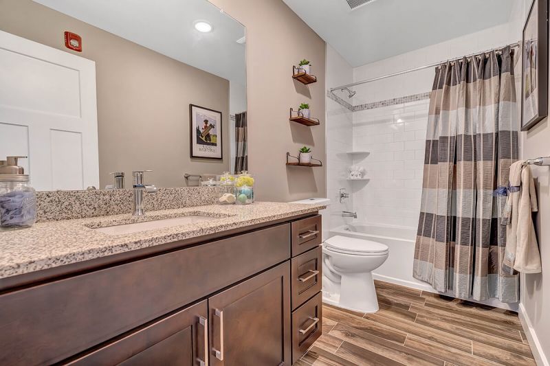 River Links interior photo of a full bathroom showing wood grain flooring, large vanity with granite counter top and huge mirror, toilet and tub with shower.