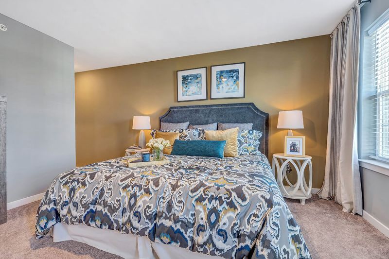 River Links interior photo of the primary bedroom showing a large bed, wall to wall carpet windows for natural light, and a hall leading to the primary bathroom