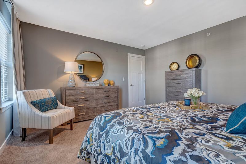 River Links interior photo of the primary bedroom showing a large bed, wall to wall carpet windows for natural light, a chair and several dressers.