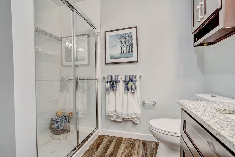 River Links interior photo of the primary bathroom showing wood grain flooring, part of the vanity and countertop, toilet with medicine cabinet above and a large walk in shower.