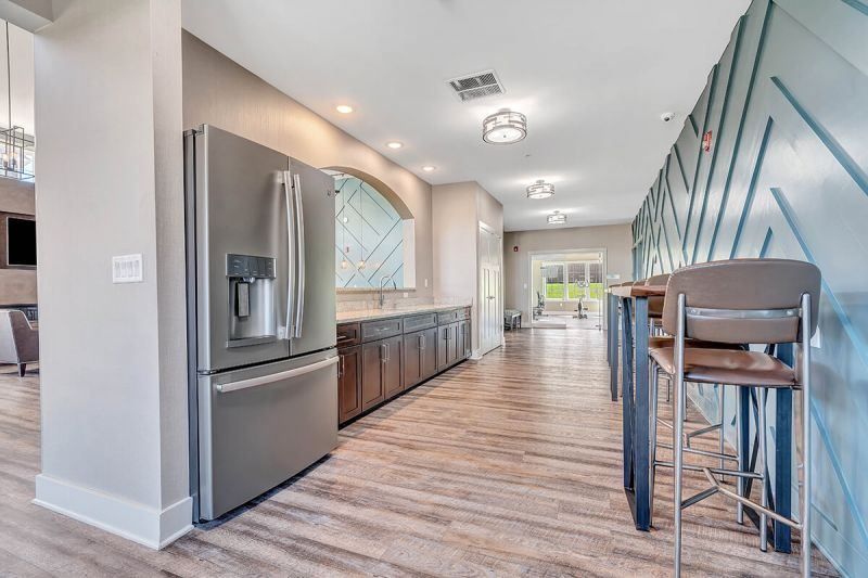 River links interior photo of the clubhouse showing a refrigerator, sink, cabinets with granite countertop, woodgrain flooring and multiple pub style seating areas.
