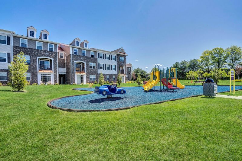 River Links exterior photo showing a playground for young children with several pieces of kids equipment, and park like benches for seating.