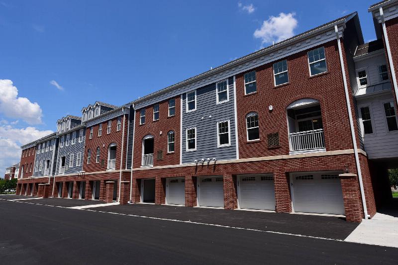 Bayonne Bay exterior photo showing three story townhome apartments with covered balconies. Also shown are garages and parking in front of each unit. 