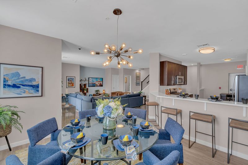 Interior photo of a model apartment at Bayonne Bay showing the dining area featuring a round table for 6. This room is open to the kitchen where you can see 4 stools for counter height dining, as well as see into the living room area. 