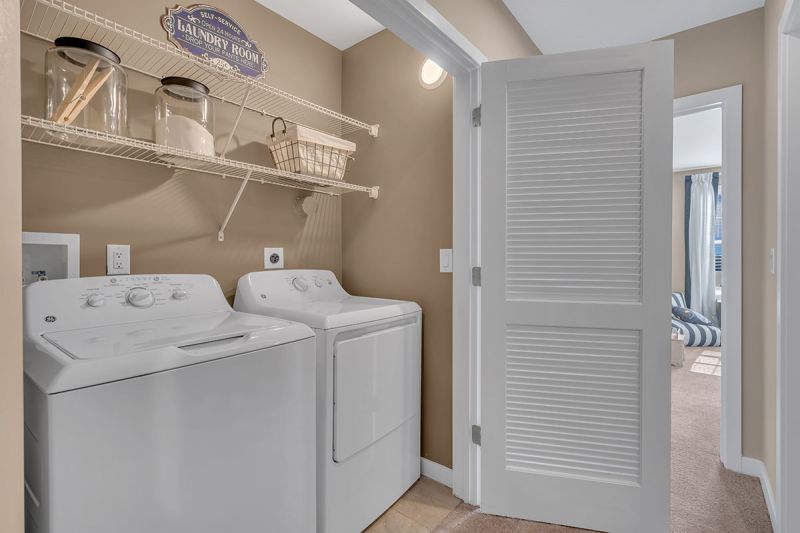 Interior photo of a model apartment at Bayonne Bay showing full size washer and dryer with shelving above and lighting inside. There are double doors to conceal the machines when not in use.