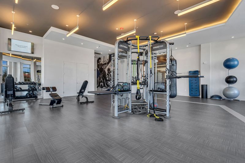 Interior photo of The Club at Bayonne Bay showing the fitness center with various stregnth training machines, free weights and benches.