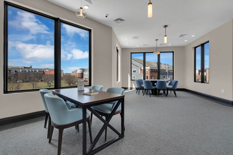 Interior photo of The Club at Bayonne Bay showing the Game Room featuring several gaming tables with chairs and large windows overlooking the community.