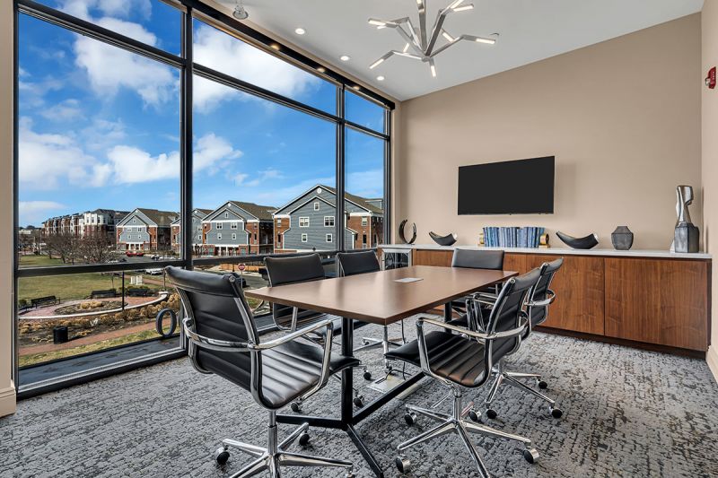 Interior photo of The Club at Bayonne Bay showing the Business Center featuring a conference table with six chairs in a comfortably decorated room with floor to ceiling widows overlooking the community.
