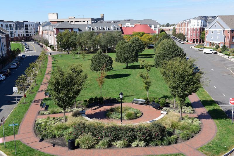 Photo of the park at Bayonne Bay featuring open green space, trees, paver walking path and a landscaped seating area.