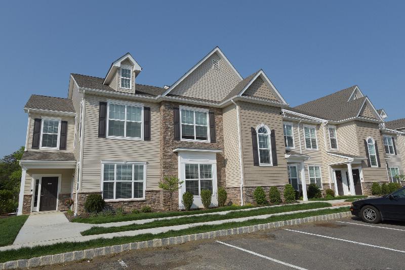 Woodhaven Meadows exterior photo shows a two level apartment building with stone and siding%2c white trim%2c black doors and shutters. Sidewalks lead to entry doors and landscape is shown around the building. 
