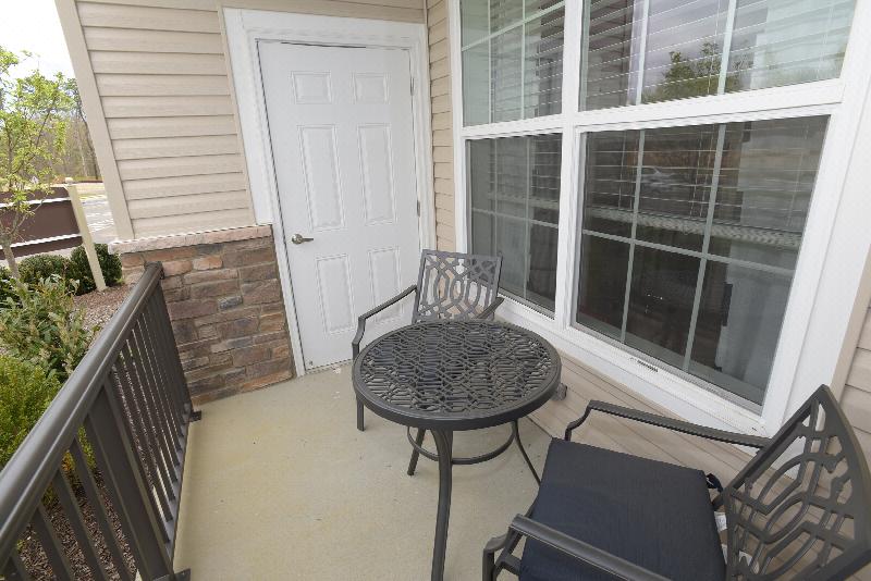 Woodhaven Meadows exterior balcony image shows a table with 2 chairs and a door leading back inside the apartment.