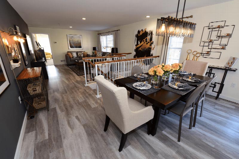 Sun Valley Plaza interior photo of the dining room showing a table for 6 with place settings. There is wood grain tile flooring and several pieces of wall art. The living room can be seen in the background.