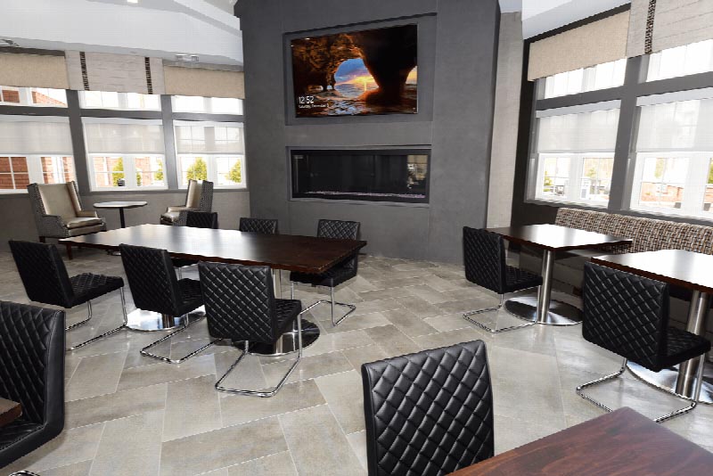 Interior photo of the community room at the Summit Club at Sun Valley. Several seating areas are shown as well as a wall mounted TV above a fireplace.