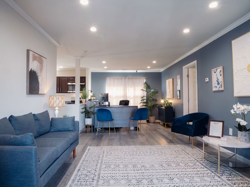 Photo of a renovated living room at Meridian Square showing new luxury vinyl plank flooring, fresh new paint, with a couch and several chairs for relaxing.