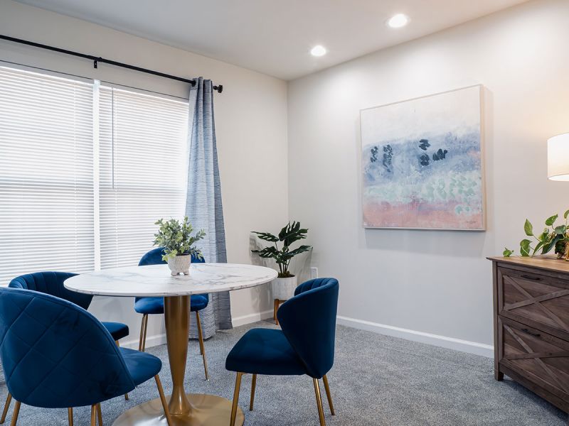 Photo of a renovated dining room at Meridian Square showing plush new carpeting, fresh new paint, table with 4 chairs and a window to allow for natural light
