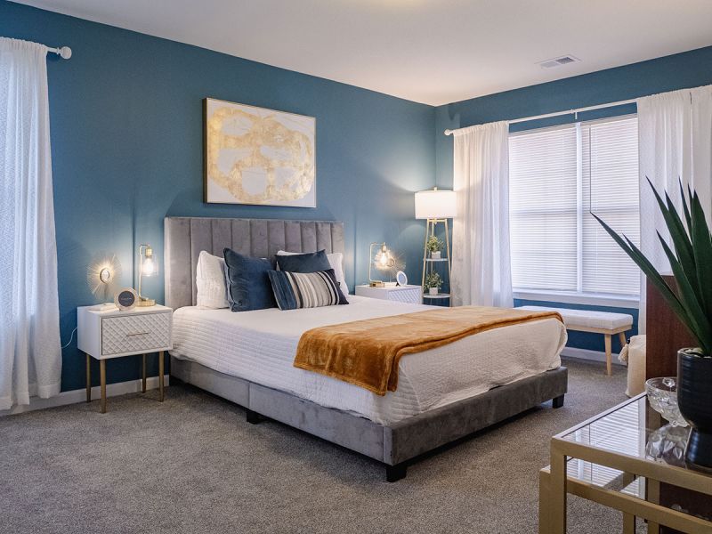 Photo of a renovated bedroom at Meridian Square showing plush new carpeting, fresh new paint, a queen size bed with 2 night stands and several windows to allow for natural light