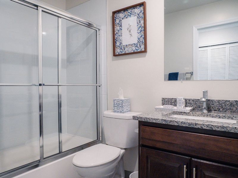 Photo of a renovated bathroom at Meridian Square showing new vanity with granite top, new toilet, new tun and shower doors