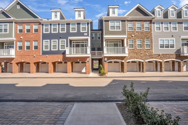 Exterior photo of a typical 3 story building at Ewing Town Center showing the exterior finishes, including red brick, mixed stone and various colors of siding with white windows and trim. Paver driveways and garages are featured.