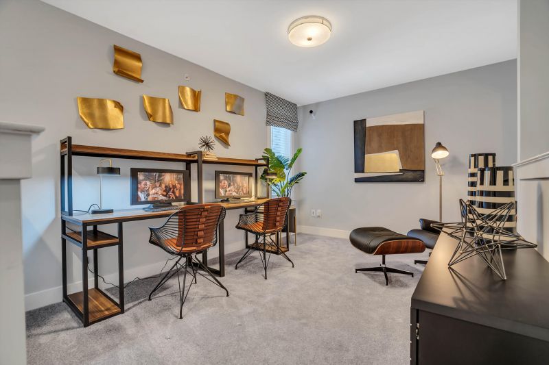 Interior photo of the den area in a typical apartment at Ewing Town Center showing a desk with 2 computers, a lounge chair, and a window allowing in natural light.