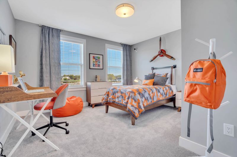 Interior photo of the second bedroom in a tyoical apartment at Ewing Town Center showing a bed, dresser, night stand and desk. There are two large windows allowing in natural light. The floor is covered with wall to wall carpeting.