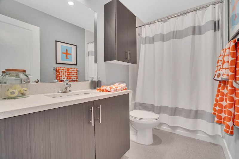 Interior photo of the second bathroom in a tyoical apartment at Ewing Town Center showing ceramic tile flooring. New cabinetry with Ceasar stone coutertops, a toilet with medicine cabinet above and a tub with shower curtain.