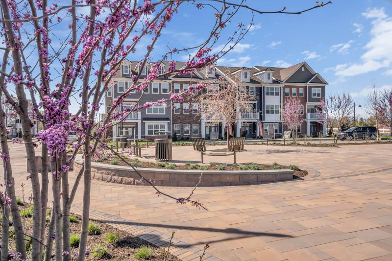 Exterior photo of the Green at Ewing Town Center showing a large seating area with multiple seating area on a paver stone patio. Many freshly planted bushes and trees can be seen around the area.