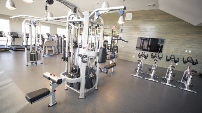 Grove Crossing gym photo showing four treadmills, three exercise bikes and various exercise equipment. There are large windows that allow natural light to enter the room.