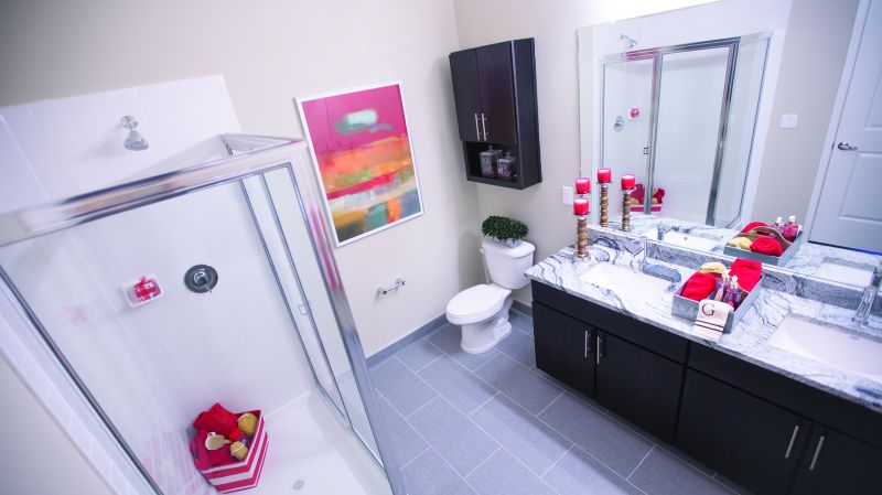 Grove Crossing bathroom photo showing a dual sink espresso vanity with a granite counter top and a mirror on the wall, a stand up shower and a toilet. There are decorations on the counter top and on the walls.