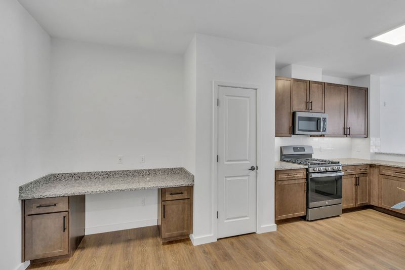 Interior photo of Amwell Terrace showing the kitchen with luxury vinyl woodgrain flooring, new cabinets with granite countertops, and a stainless steel appliance package and a built in desk.