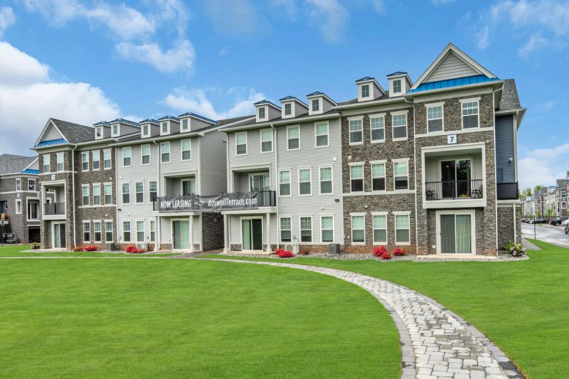 Exterior photo of Amwell Terrace showing a 3 level apartment building with gray siding, mixed stone and white trim. 