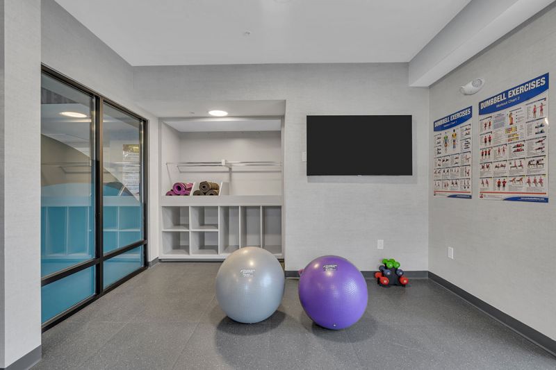 Interior photo of the movement studio at Amwell Terrace showing small weights, exercise balls, an open floor and a large screen tv on the wall.