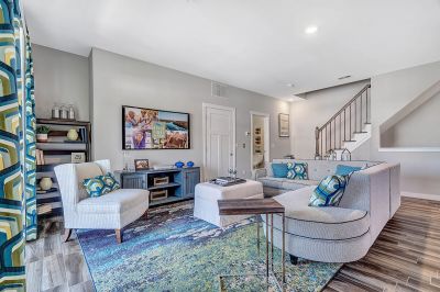 Amwell Terrace interior photo of the living room, showing wood grain flooring, comfortable couches and chairs, a wall mounted tv. Stairs to the upper level are shown in the background.