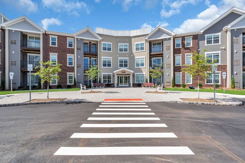 Exterior photo of Meadows at Montgomery showing the main building entryway with a large paver patio leading up to the doors.