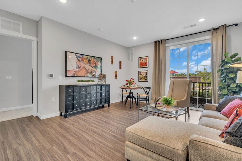 Interior photo of a Meadows at Montgomery apartment showing the living room area with luxury woodgrain vinyl tile flooring, a sitting area, wall mounted tv with console, and cafe table displayed.