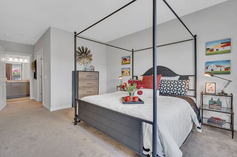 Interior photo of a Meadows at Montgomery apartment showing the primary bedroom showing a queen sized bed with night stand, and lush carpeting leading to the primary bathroom