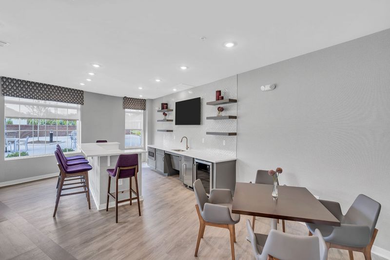 Interior photo of one of the community spaces at Meadows at Montgomery showing a luxury vinyl tile floor and multiple seating areas and a large screen TV mounted on the wall.